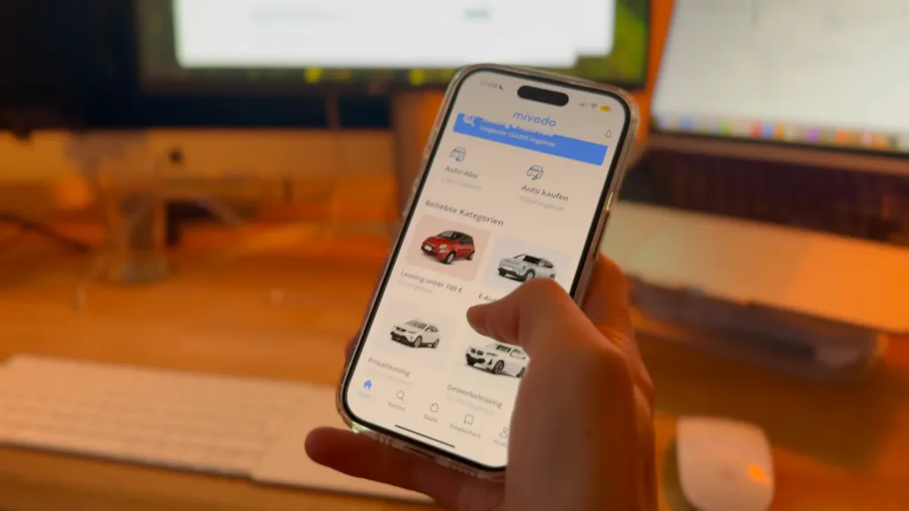 Hand hält ein iPhone mit der Mivodo-App, die Leasingangebote für Autos zeigt